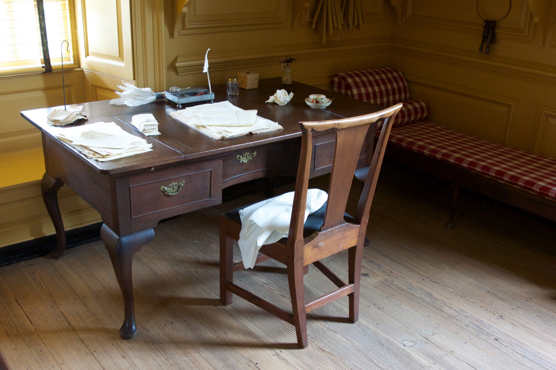 Antique wooden writing desk sits in the corner of a colonial work office.